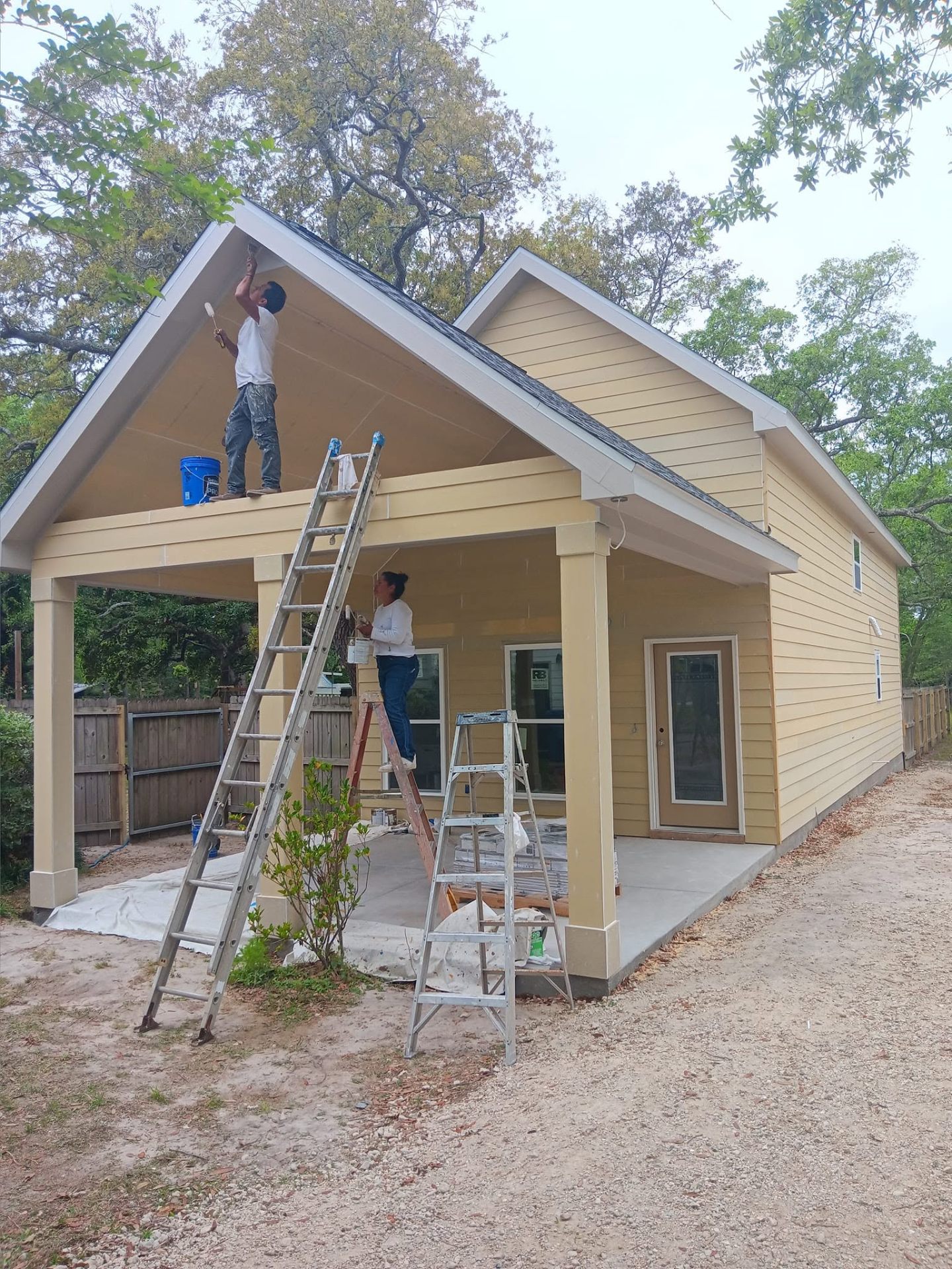 Painters on ladders repainting yellow siding home